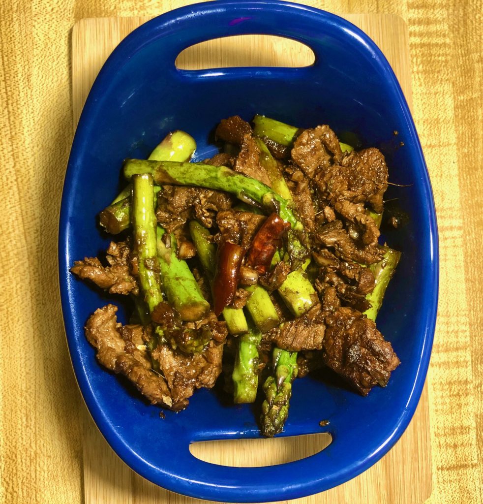 steak and asparagus stirfry with thai chili pepper plated in royal blue bowl on oak counter