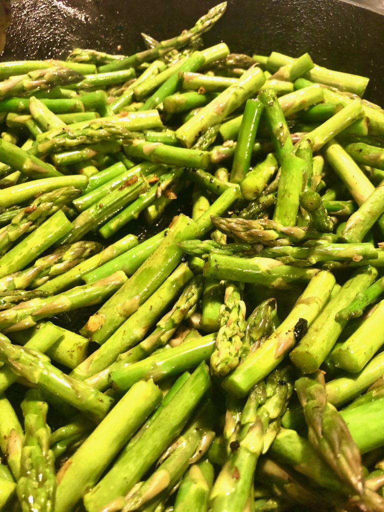 beautiful vibrant green asparagus frying in black cast iron skillet