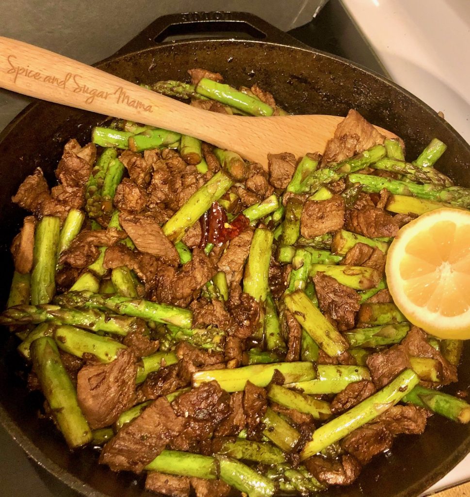 steak and asparagus stirfry with thai chilis in black skillet pictured with sliced lemon wedge and wooden serving spoon