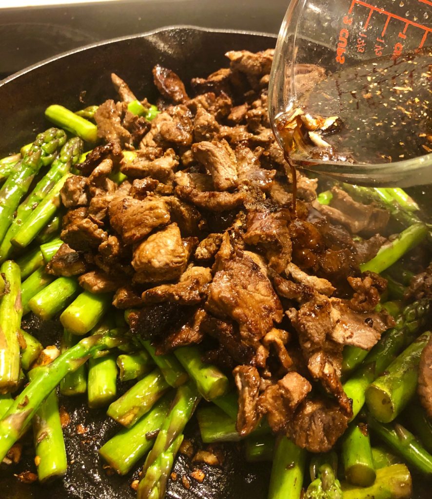 asparagus and steak stir-frying in skillet with marinade being poured in