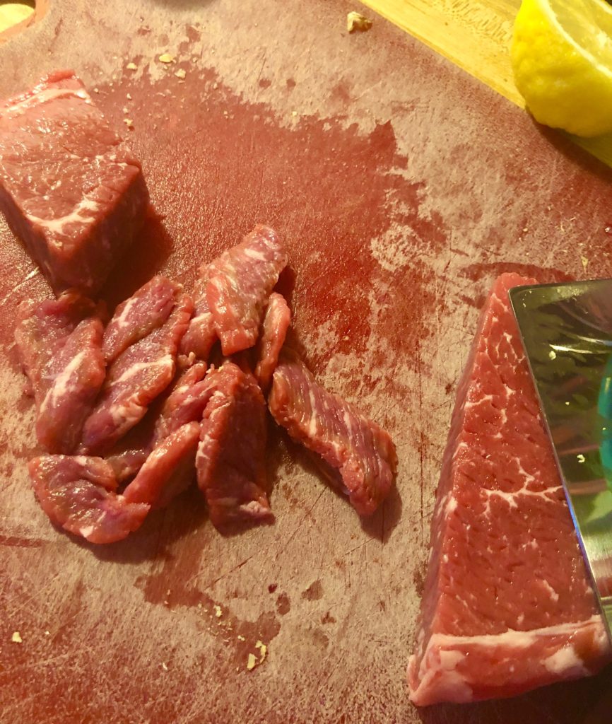 flank steak being sliced on red cutting board pictured with knife and lemon wedge in the background