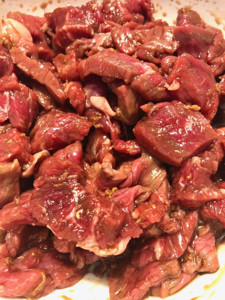 soy sauce and ginger marinated flank steak in white mixing bowl