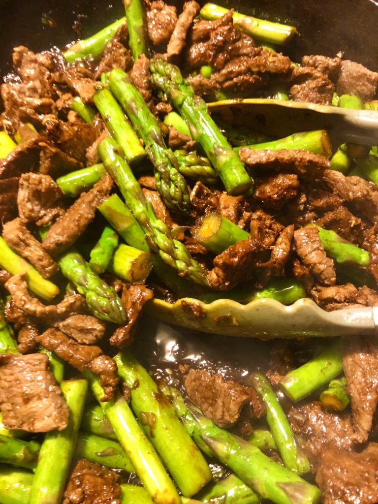 steak and asparagus being stir fried in marinade