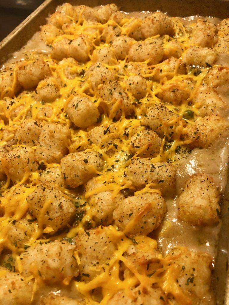 Shepherd's pie tater tot casserole in baking pan with melted cheddar cheese and dried parsley over the top
