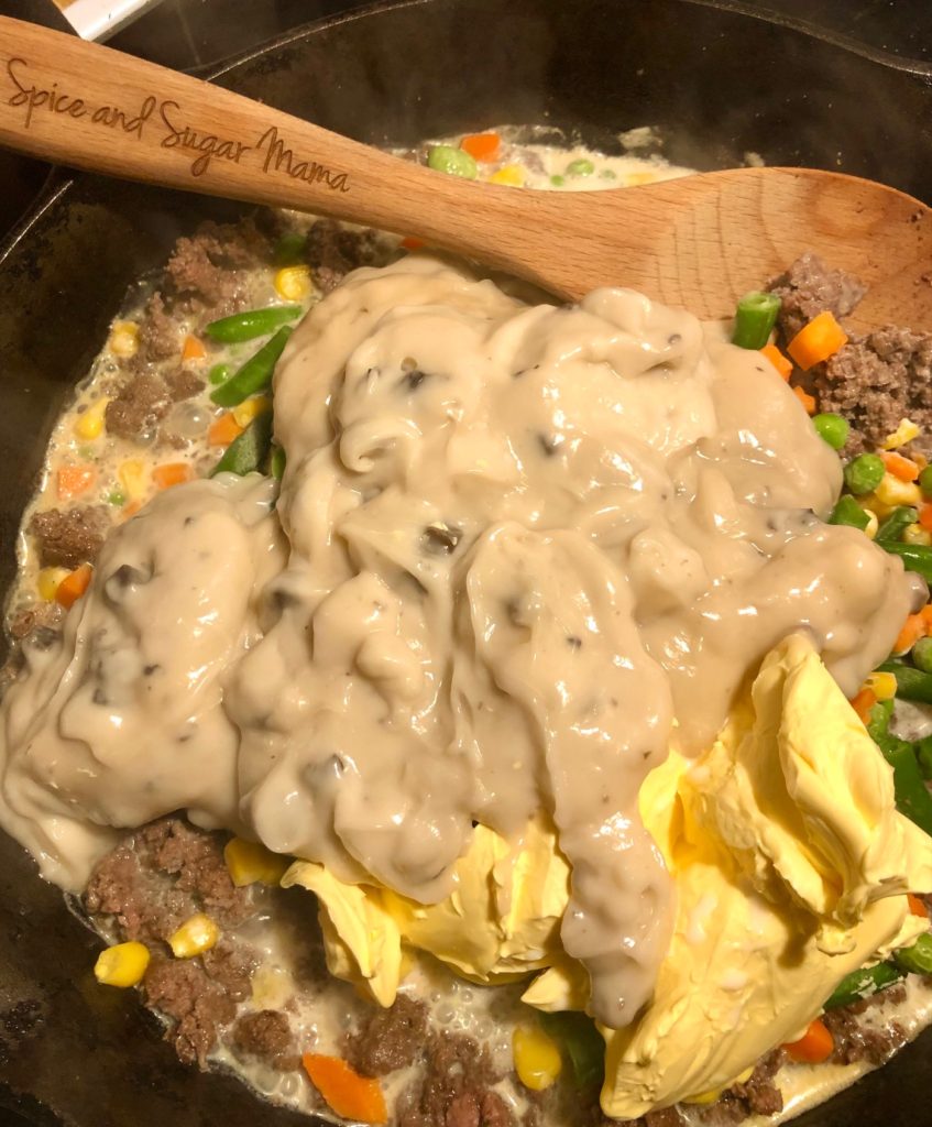 ground beef, cream of mushroom soup, mixed veggies, butter and milk in black cast iron skillet pictured with wooden spoon