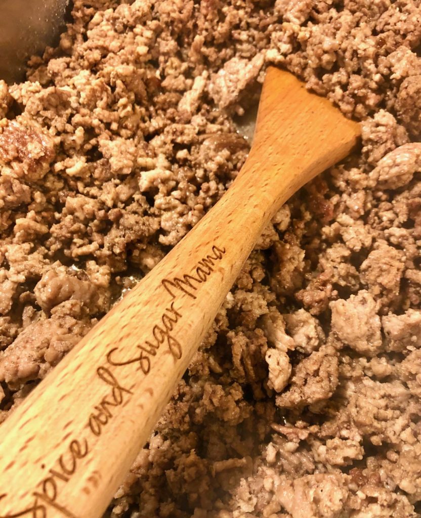 browning beef in skillet using wooden spoon with spice and sugar mama logo