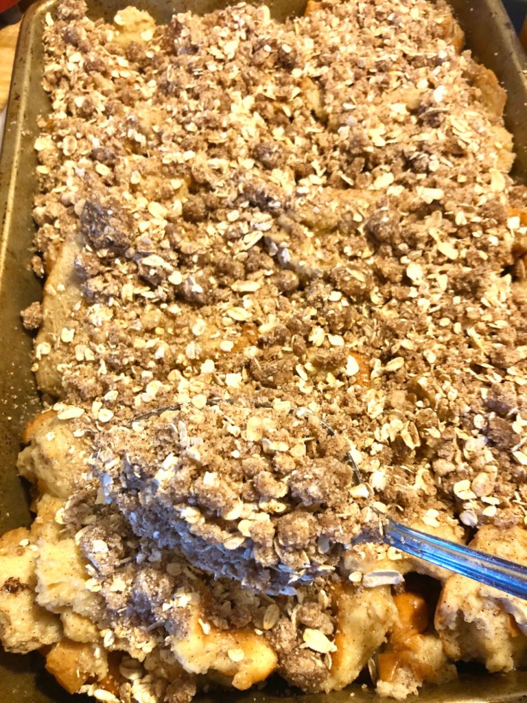 adding crumb cinnamon oat topping to french toast casserole with silver spoon