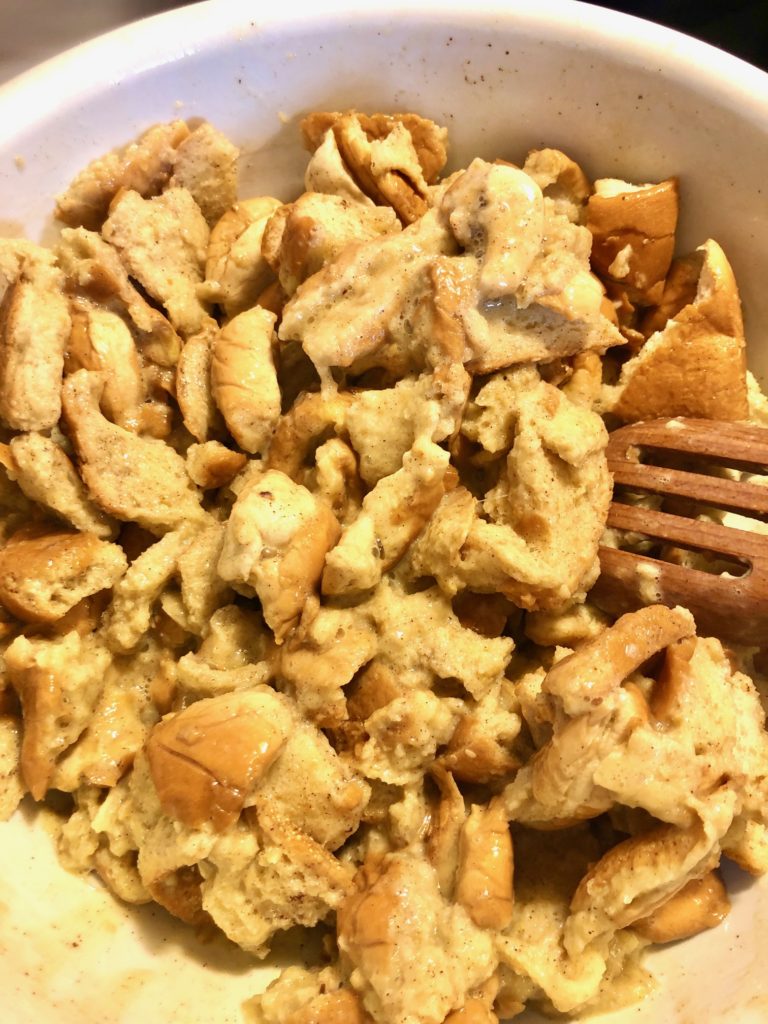 leftover day old bread being mixing with french toast egg mixture with wooden spoon in large white mixing bowl