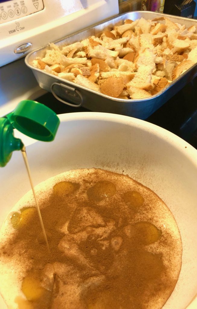 adding maple syrup to egg mixture for French toast. a silver baking pan with torn bread is in the background