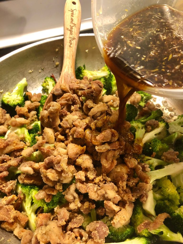 fried chicken and broccoli in frying pan with Orange and soy sauce being drizzled into the pan
