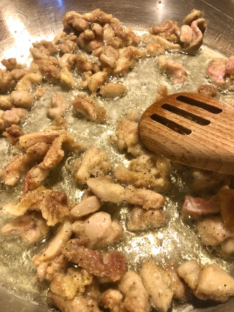 cornstarch coated boneless skinless chicken frying in silver frying pan and being stirred with wooden spoon