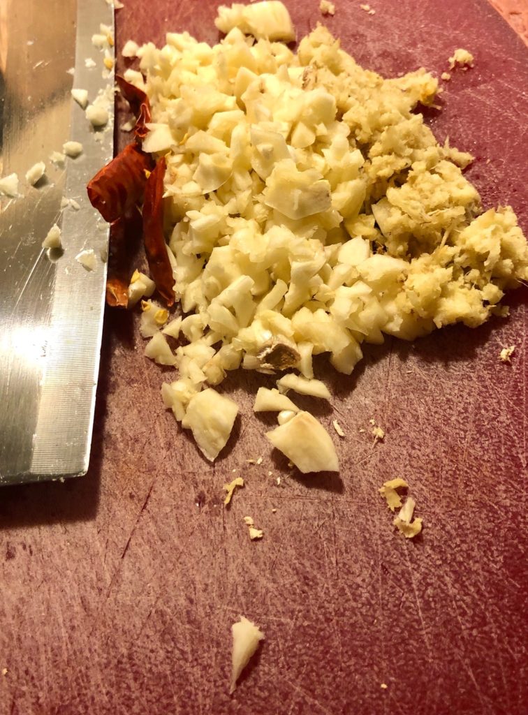 garlic, ginger and Thai chilis on red cutting board with butcher knife