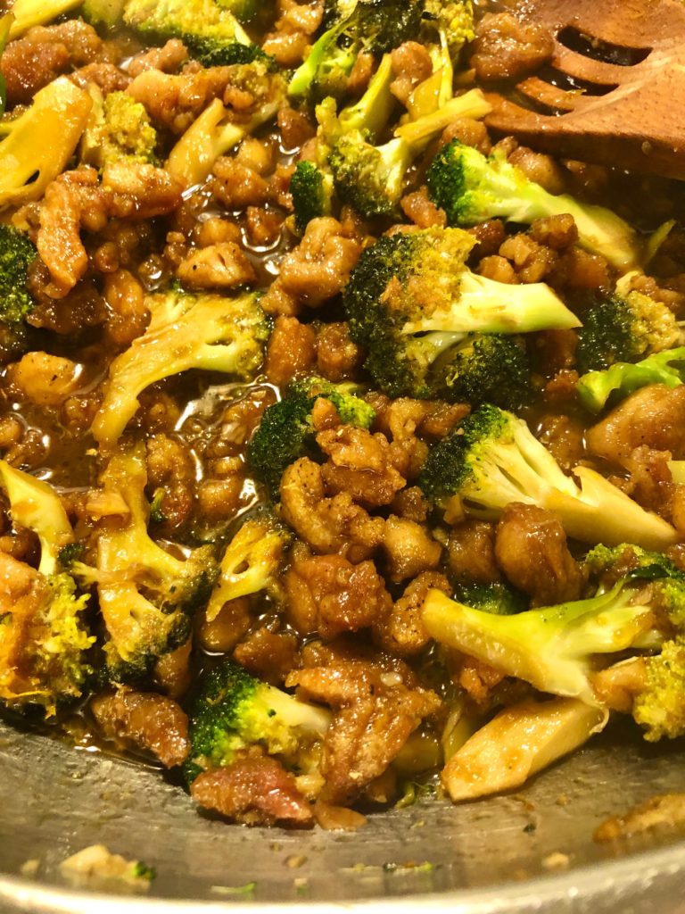 orange chicken with broccoli in silver pan with wooden spoon