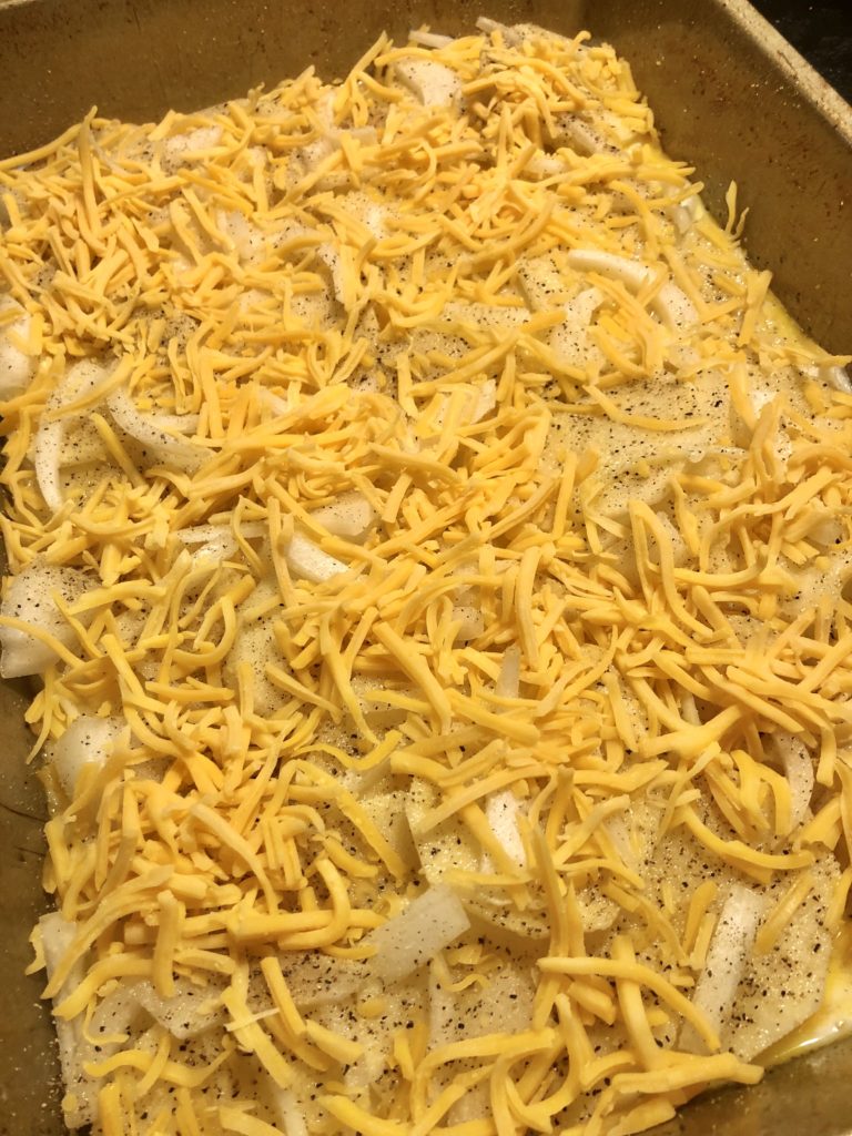 potatoes au gratin with onion and garlic topped with shredded cheddar cheese in baking dish