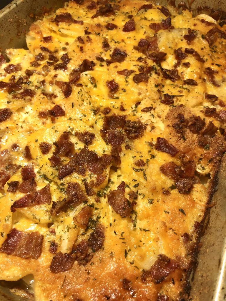 potatoes au gratin with bacon and melted cheddar cheese over the top in silver baking dish