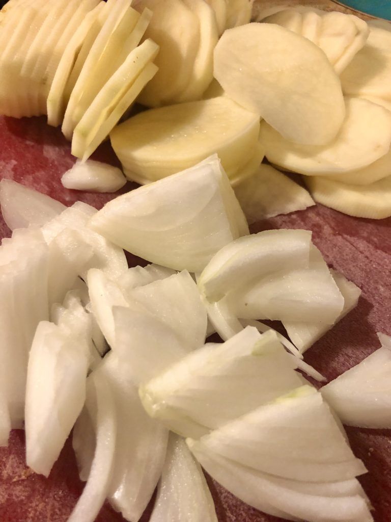thinly sliced potatoes and onion on red cutting board