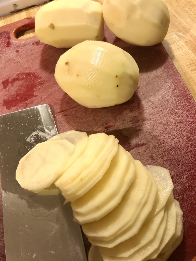 thinly slicing russet potatoes on a red cutting board
