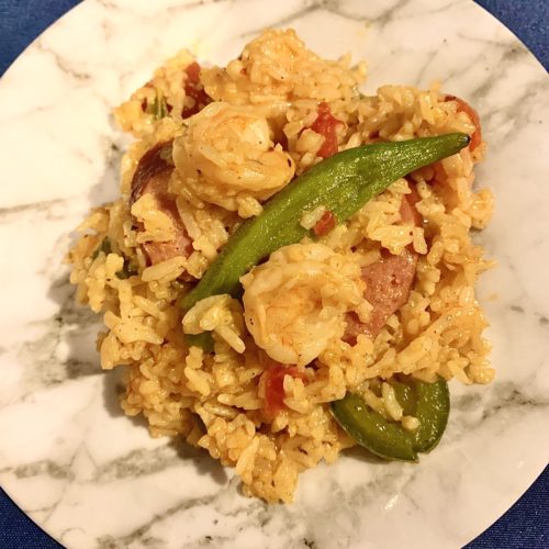 gumbo skillet rice with kielbasa, shrimp and okra on white marble plate with navy background