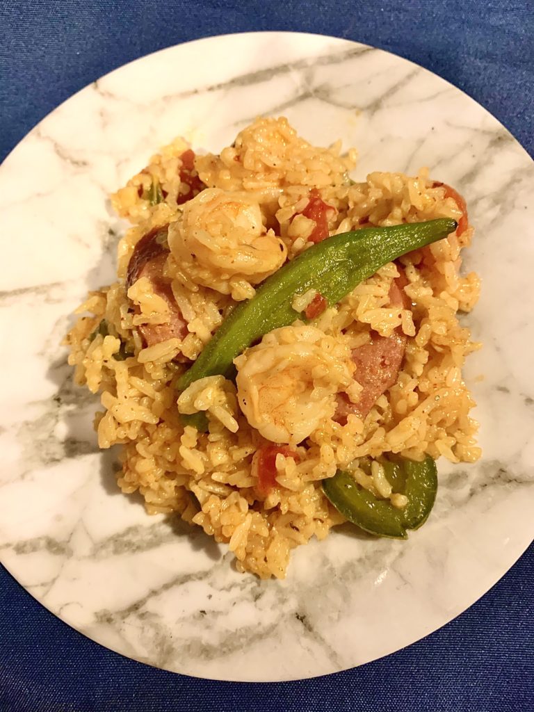 gumbo skillet rice with kielbasa, shrimp and okra on white marble plate with navy background