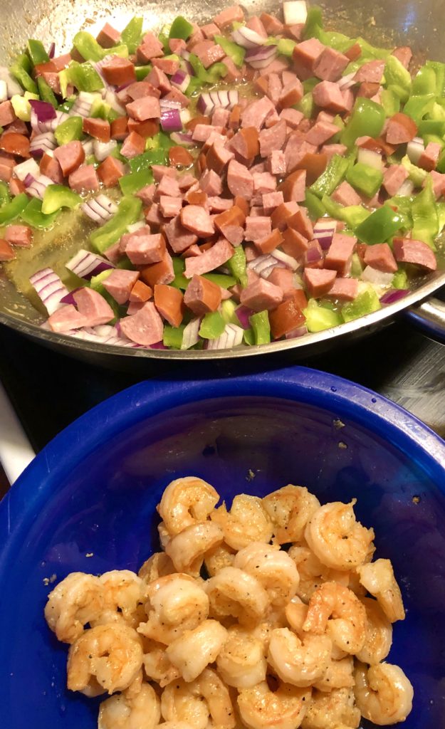 kielbasa, green pepper, onion and garlic frying in skillet. shrimp that has already been cooked is in a blue bowl beside the pan.