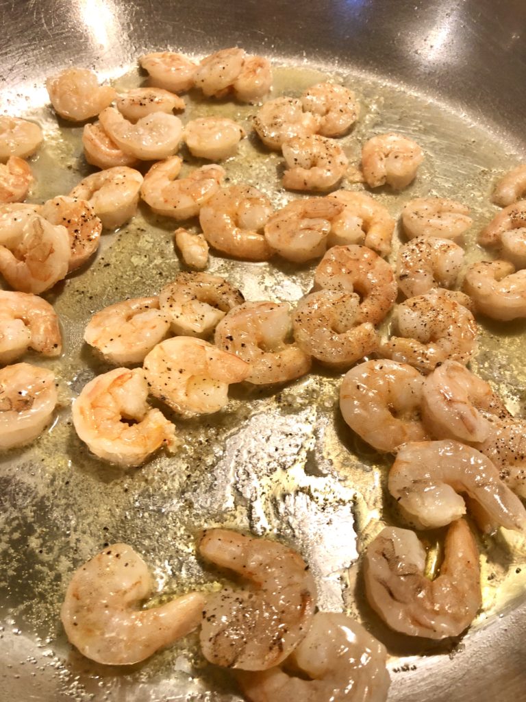 shrimp frying in large skillet with butter, salt and black pepper