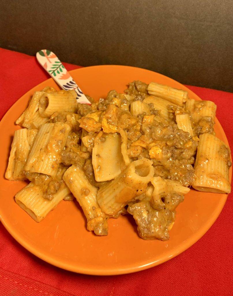 cheesy taco rigatoni with ground beef plated on orange plate with floral fork on red fabric