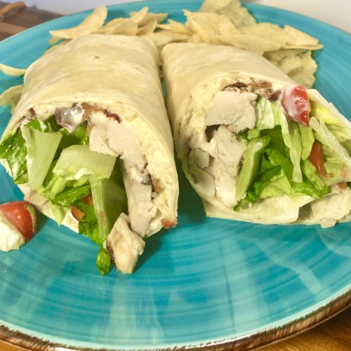 chicken Caesar wraps on flour tortillas with bacon pictured on vibrant blue plate with potato chips in the background