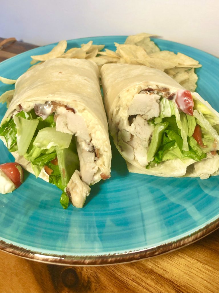 chicken Caesar wraps on flour tortillas with bacon pictured on vibrant blue plate with potato chips in the background
