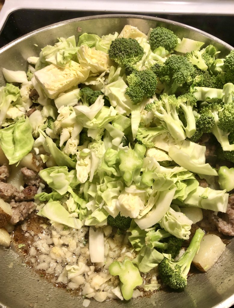 cabbage, broccoli, potatoes, sausage and garlic frying in large silver pan