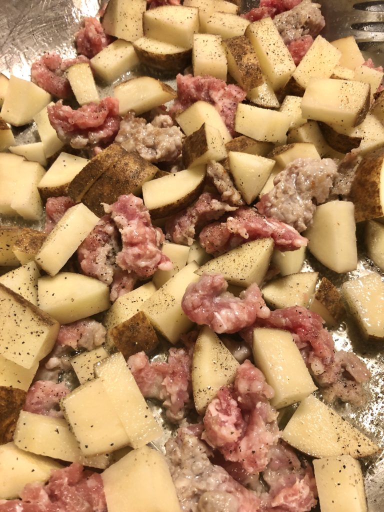 Italian sausage that has been removed from the casing and russet potatoes frying in vegetable oil in a silver frying pan