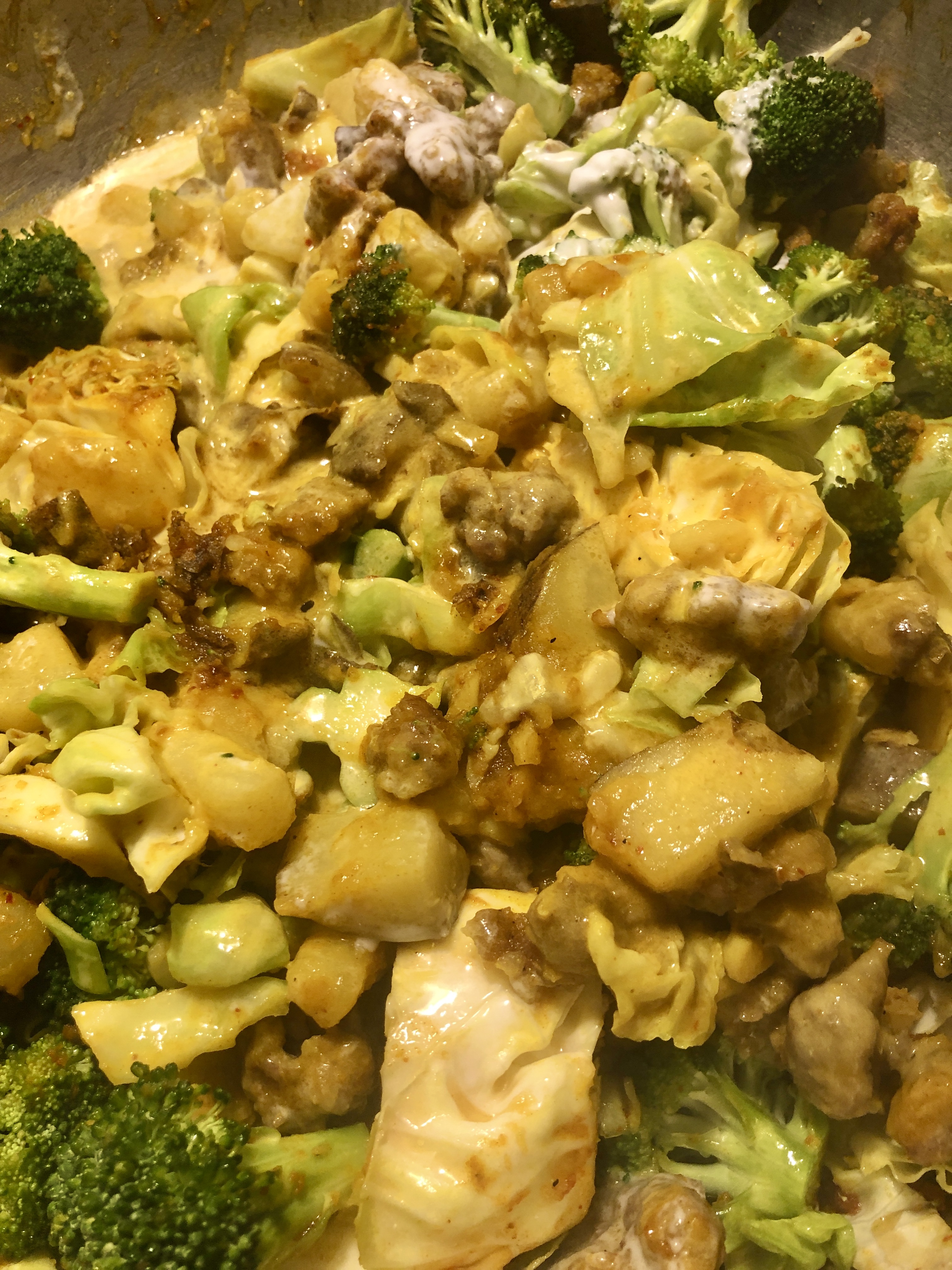 adding coconut milk into pan of sausage, potatoes, cabbage and broccoli with Thai curry spices