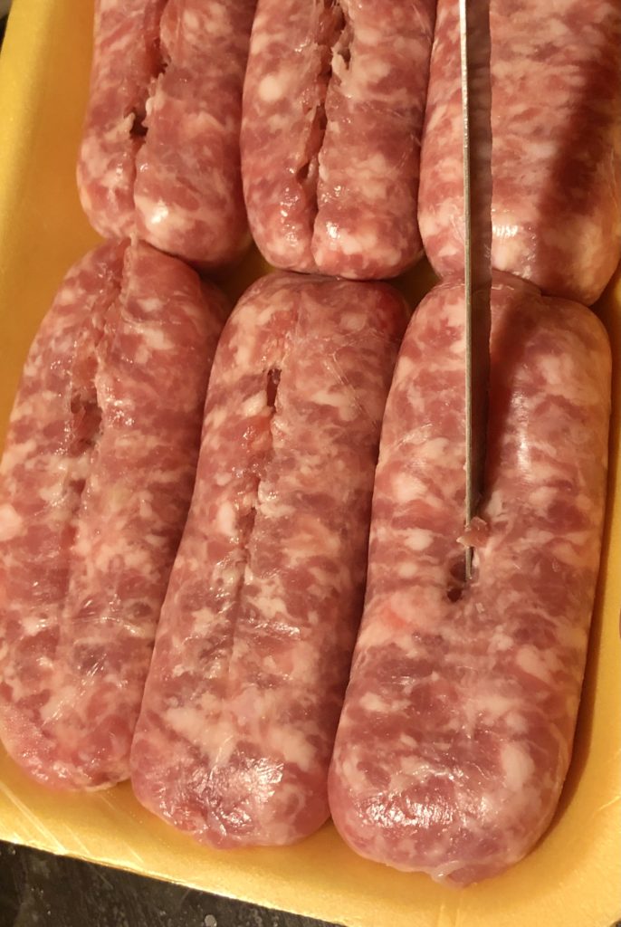 slitting Italian sausage down the middle with a knife so that the casing may be removed