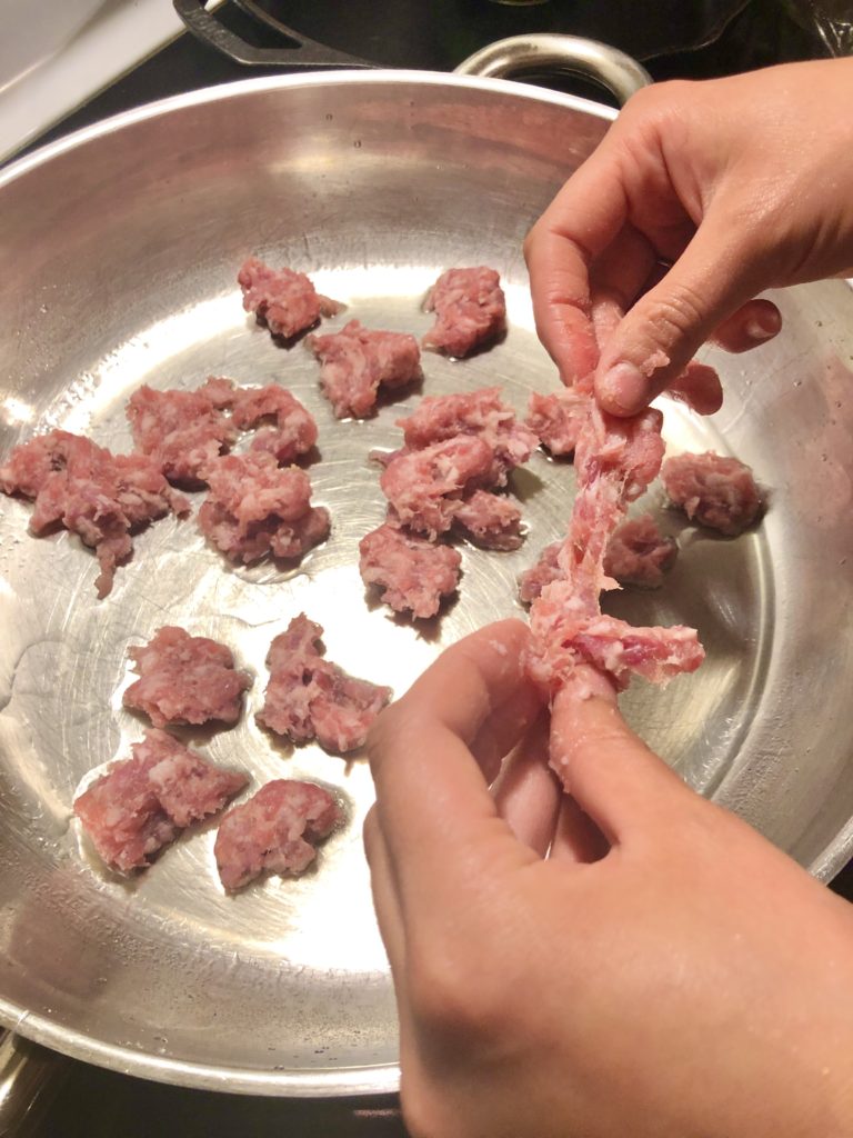 adding Italian sausage that has had the casing removed into a frying pan
