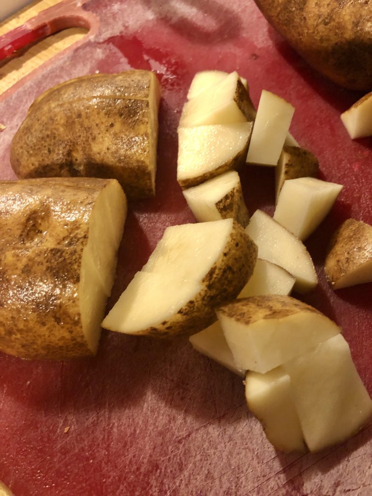 slicing a russet potato into small cubes on a red cutting board