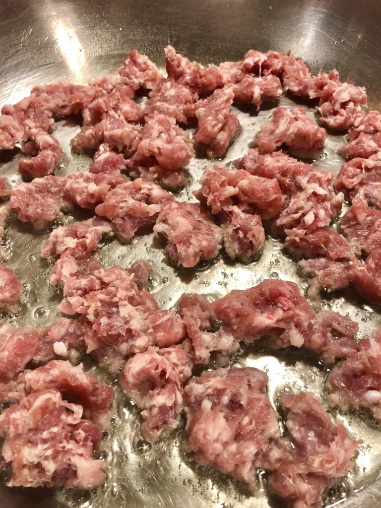 Italian sausage frying in silver frying pan after being removed from the casing