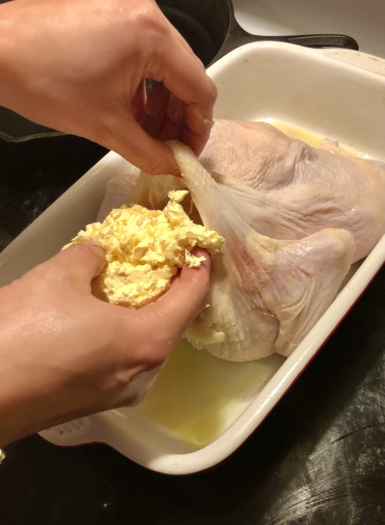 adding butter spread and minced garlic mixture underneath the skin of a whole roaster chicken. the chicken is in a roasting pan with olive oil