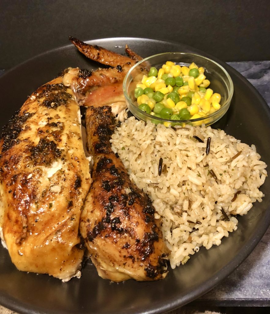 lemony oven roasted chicken carved and plated on black plate. Breast, drumstick and wing plated with wild rice and a side of corn and peas