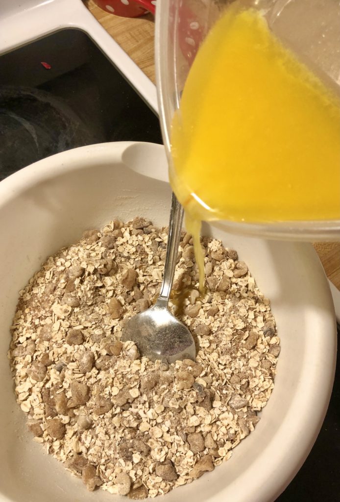 pouring butter into white mixing bowl with the crisp topping ingredients including sugar, flour, cinnamon and oats