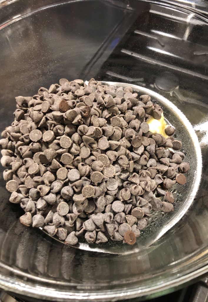 chocolate chips and butter being melted in glass bowl of double boiler