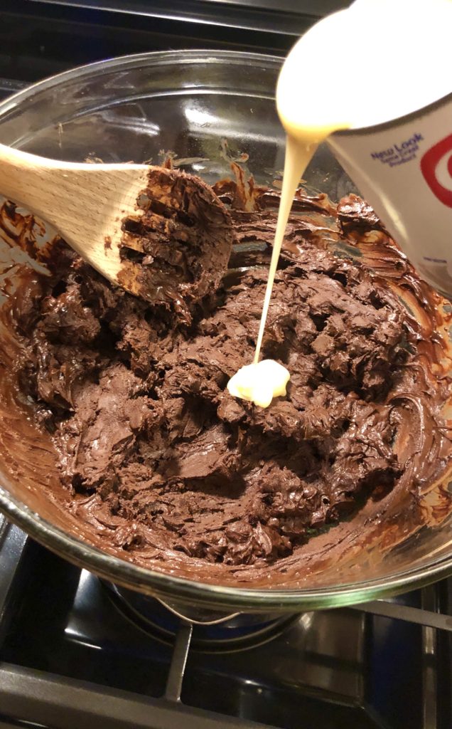 sweetened condensed milk being poured into melted chocolate in glass bowl over double boiler