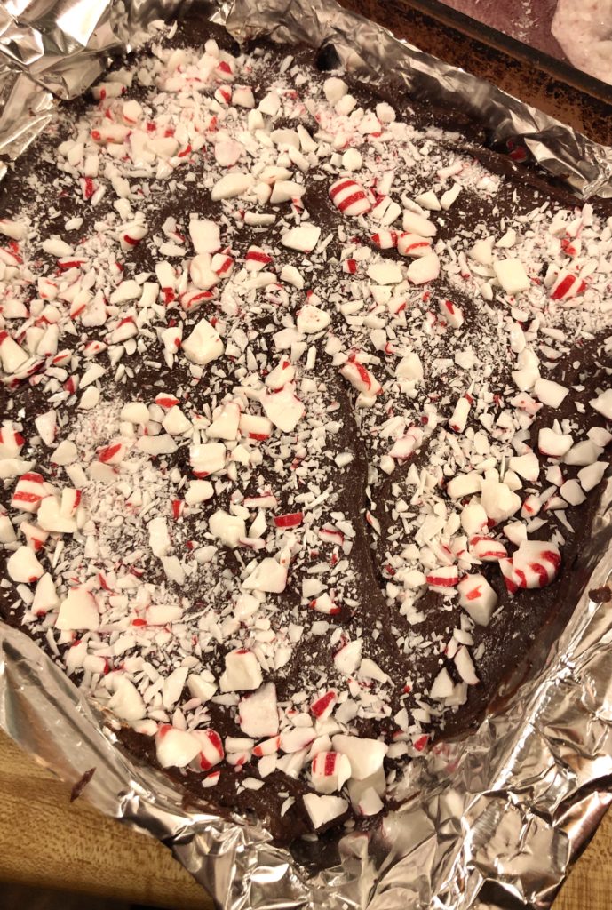 adding crushed starlight peppermint candies to the top of dark chocolate peppermint fudge in 8x8 pan