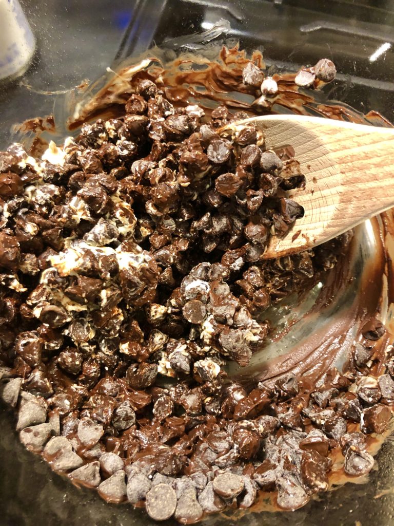 stirring melting chocolate chips with wooden spoon over double boiler