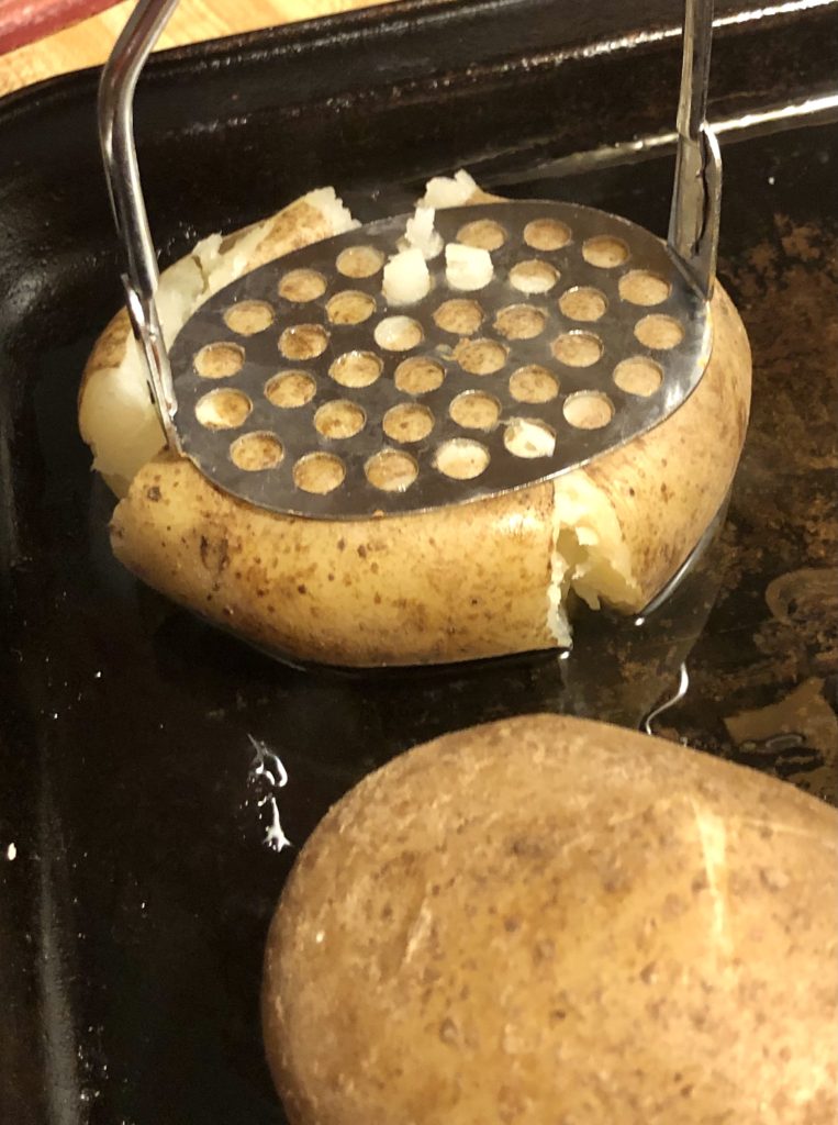 smashing a russet potato lightly with a potato hand masher on a pan
