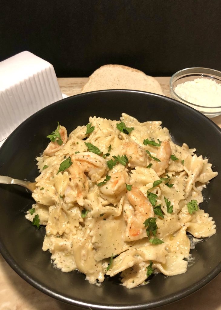 cajun shrimp pasta pictured in black matte bowl with fork in bowl. Pasta is garnished with fresh parsley. Bread, a butter dish and a glass ramiken with grated parmesan cheese are in the background