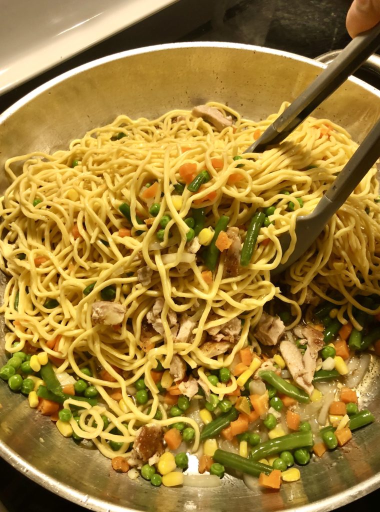 large silver skillet with chicken lo mein noodles and veggies being tossed and mixed together