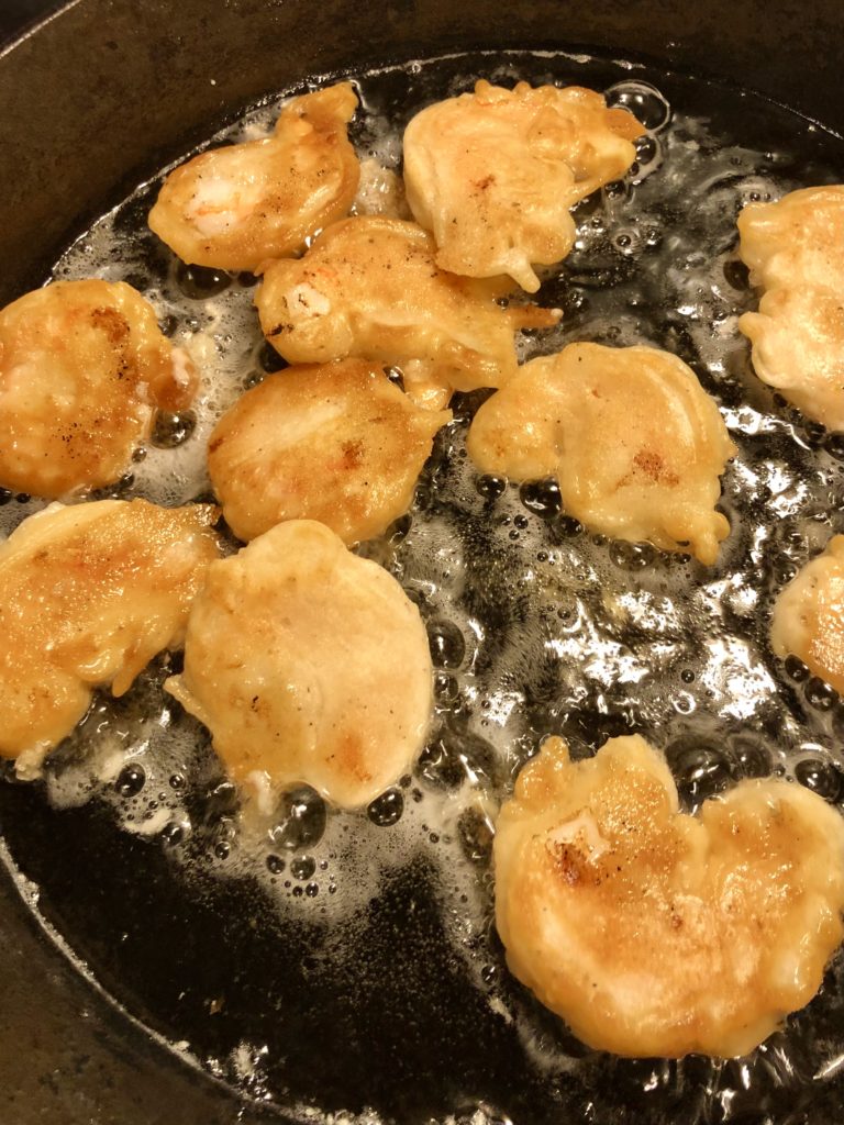 battered Chinese fried shrimp frying until golden brown in vegetable oil in cast iron skillet