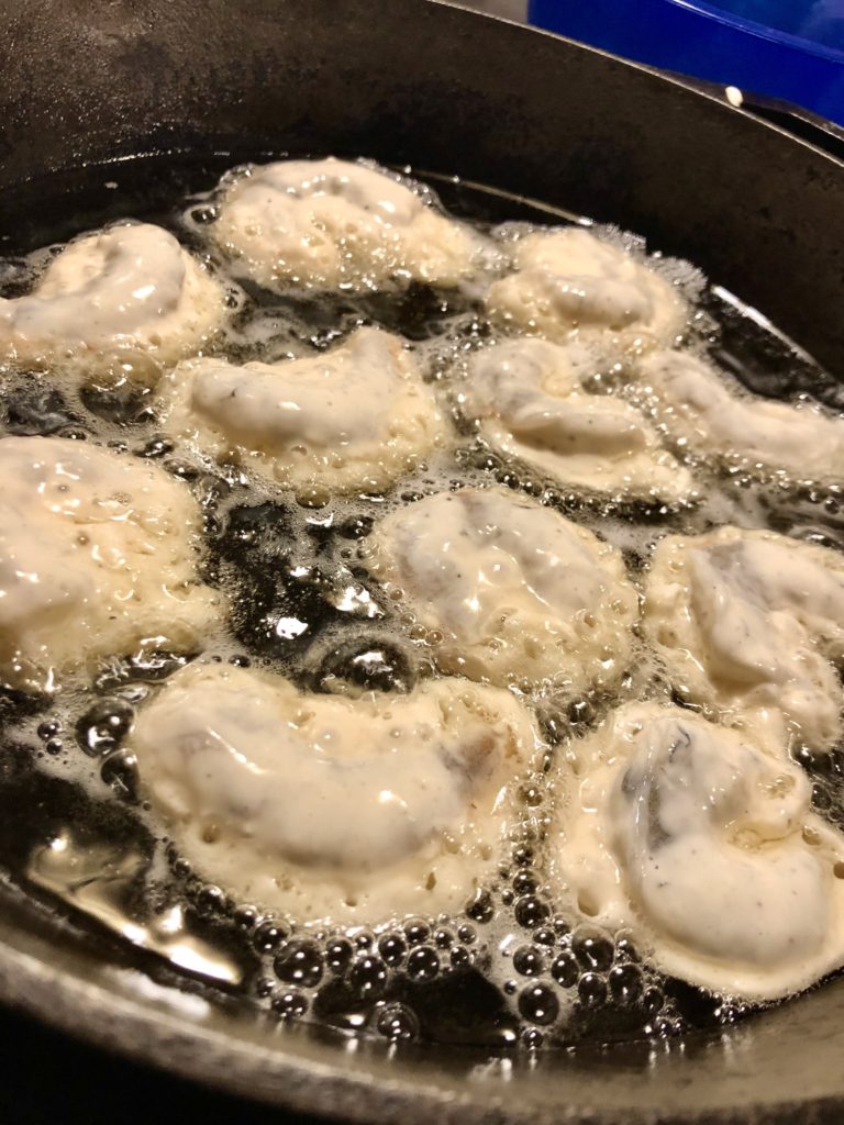 Ten jumbo shrimp battered and dropped in oil in skillet for frying