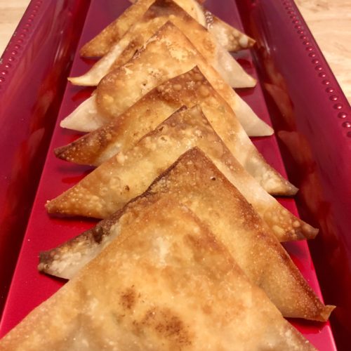 seven fried crab rangoons pictured on long red rectangle plate with a clear ramiken in the background filled with a dipping sauce