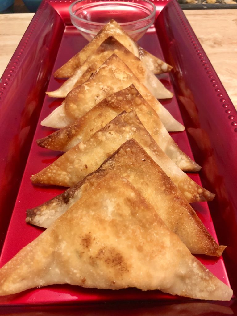 seven fried crab rangoons pictured on long red rectangle plate with a clear ramiken in the background filled with a dipping sauce