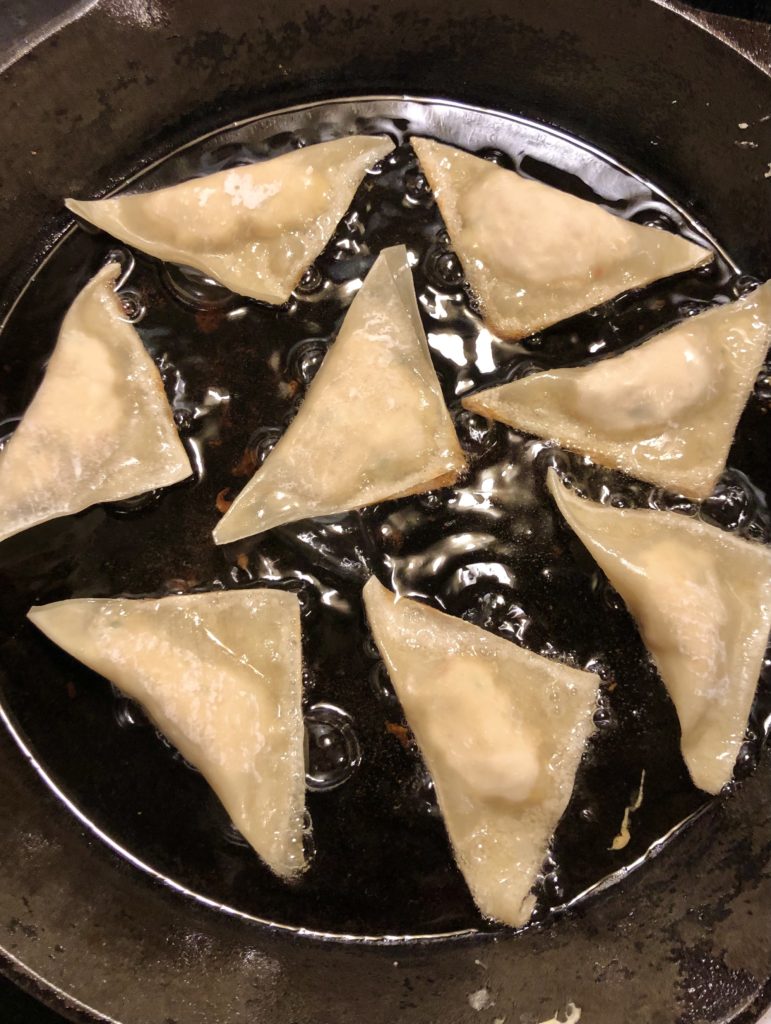 eight crab rangoons being fried in vegetable oil in cast iron skillet